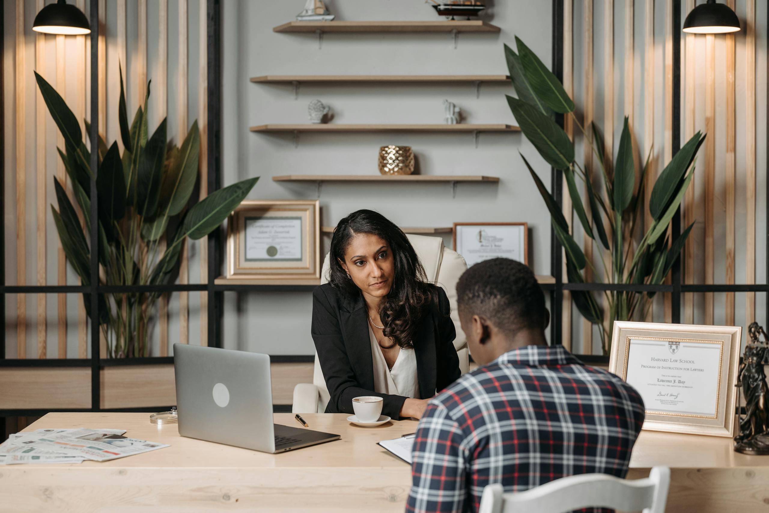 Two people engaged in discussion in a modern office with certificates and plants.