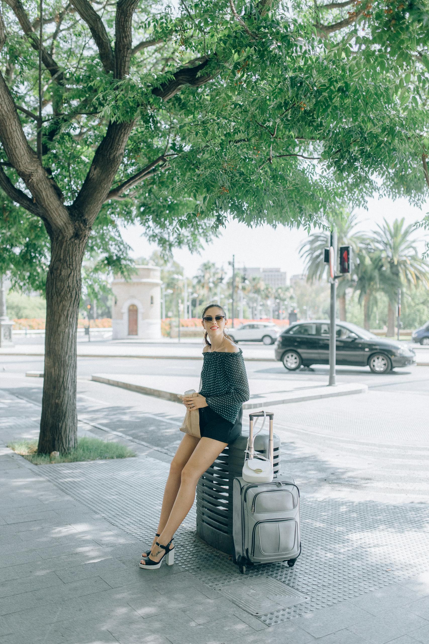 Woman sitting with luggage on sunny city street, enjoying travel.